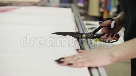 非常接近一个女性卖家用黑色剪刀切割浅色组织的镜头布料在上面视频的预览图