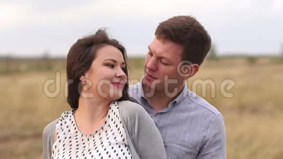 幸福的丈夫温柔地拥抱着他怀孕的妻子站在夕阳下的田野里视频的预览图