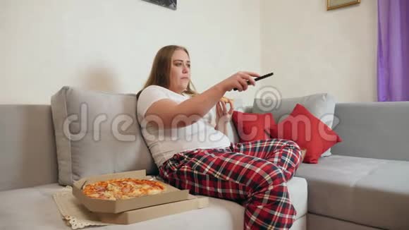 超重的女人吃披萨看电视视频的预览图
