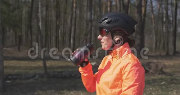 戴着头盔和太阳镜的女人从瓶子里喝水女性自行车运动员饮用等渗饮料的肖像与女孩亲近视频的预览图
