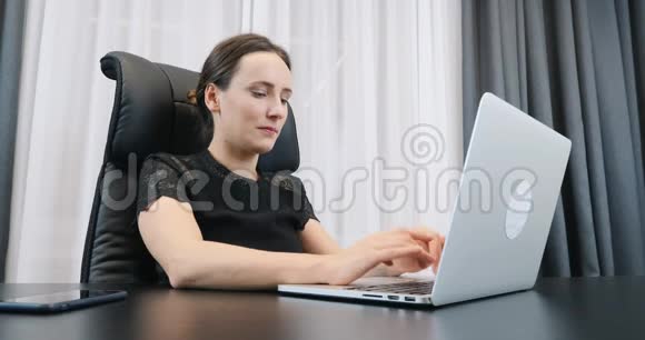 女商人在办公室工作白人年轻女性在笔记本电脑键盘上打字看着屏幕穿黑色衣服的女人视频的预览图