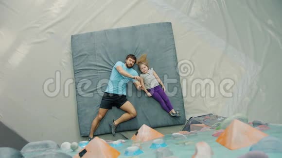 父亲和女儿躺在攀岩场的垫子上谈论攀岩视频的预览图