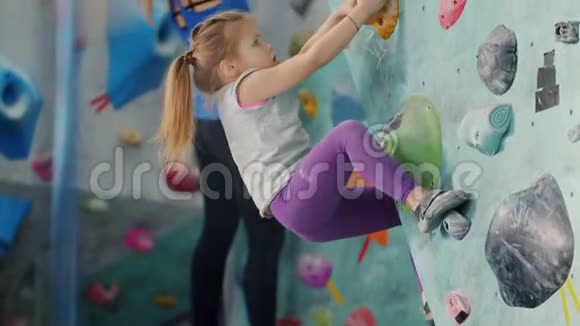 可爱的小女孩爬上五颜六色的人造墙训练室内健身房视频的预览图