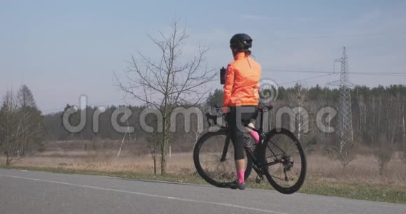 女人正在喝水准备骑自行车戴着头盔的女自行车运动员从瓶子里喝饮料开始骑自行车训练视频的预览图