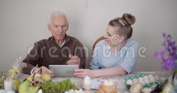 老人退休微笑老人与孙女交谈同时使用数字平板电脑视频的预览图