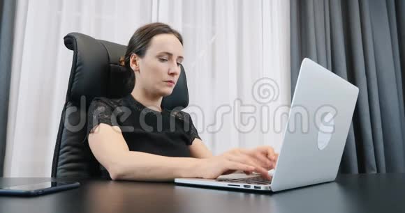在办公室用笔记本电脑工作的女性女人在电脑键盘上打字穿着黑裙子的女老板坐在办公桌前视频的预览图