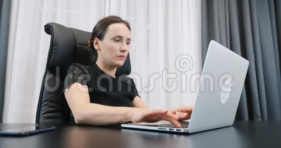 年轻女性在笔记本电脑上工作和在键盘上打字的肖像自信的女商人穿着黑色连衣裙坐在办公室里铁视频的预览图