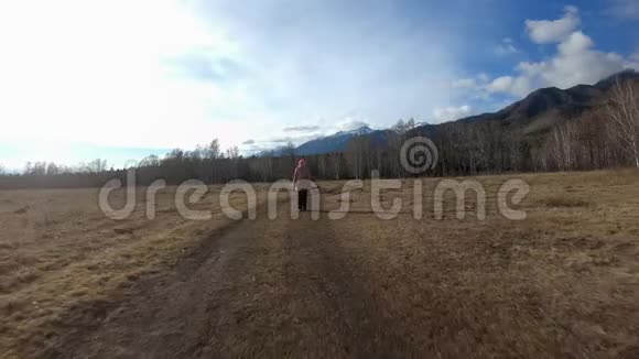 秋天女孩走在山脚下的田野里的乡间小路上视频的预览图