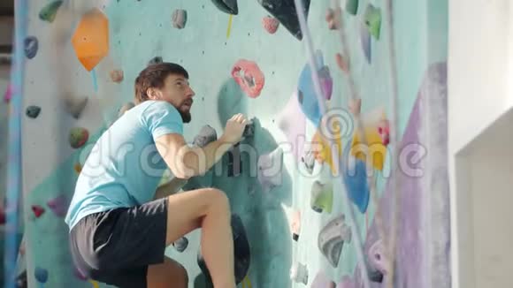 一个人在室内攀爬爬上人造墙抓起五颜六色的岩石视频的预览图