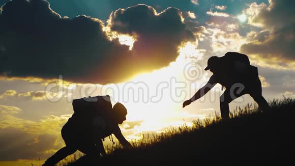 在两个登山者之间帮忙的剪影山顶上有两个徒步旅行者一个人帮助一个人爬上一个纯粹的地方视频的预览图