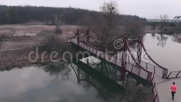 女子独自过桥鸟瞰女性早上在公园里和河一起慢跑穿鲜艳运动服装的女孩视频的预览图