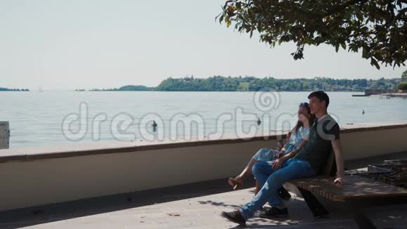 情侣坐在长廊树下的长凳上欣赏加德纳湖的景色视频的预览图