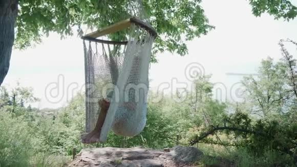 光着脚的女孩在加德纳湖畔的露营地的吊床上休息阳光明媚的一天视频的预览图