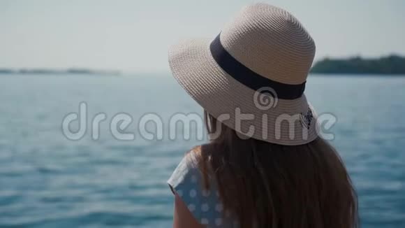 在阳光明媚的日子里戴着草帽的女孩坐在湖岸上湖色惊人视频的预览图