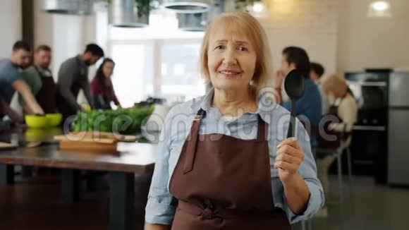 穿着围裙的老妇人在烹饪课上微笑着看镜头的画像视频的预览图