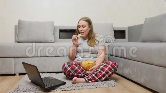 超重女孩吃薯片看着笔记本电脑屏幕视频的预览图