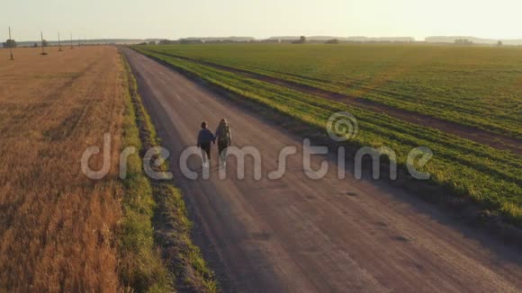 远足者和旅行者一个带着女孩的年轻人肩上扛着背包沿着播种的麦田行走视频的预览图