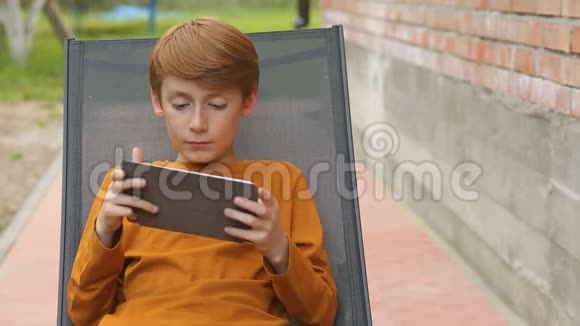 坐在阳光休息室里的男孩在平板电脑上玩游戏视频的预览图