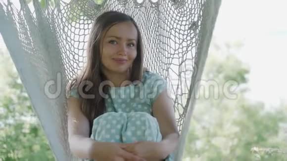 年轻女子在吊床上放松的肖像微笑着看着镜头阳光明媚视频的预览图