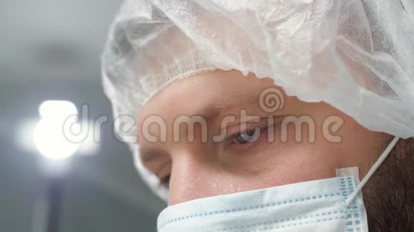 戴着外科口罩的疲惫男子外科医生低头看着病人然后站在班长或助手旁边行动视频的预览图