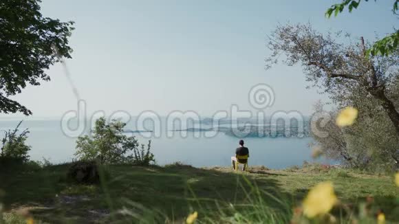 年轻人坐在山上的黄椅子上休息看着美丽的湖景视频的预览图