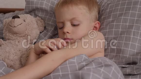 一个生病的小男孩躺在床上拿着温度计和泰迪熊视频的预览图