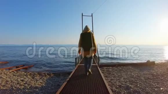 戴着背包的女孩沿着金属码头走向大海视频的预览图