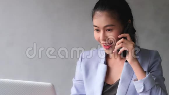 年轻的亚洲妇女拿起电话与客户谈论工作进展视频的预览图