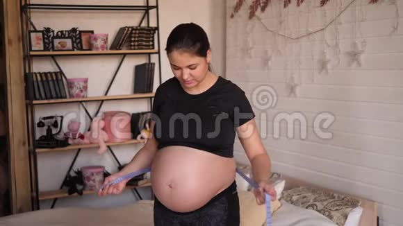 孕妇手持厘米卷尺测量腹部的肖像视频的预览图