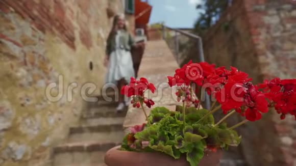 穿裙子的女孩从老城的楼梯上下来前景中的红花视频的预览图