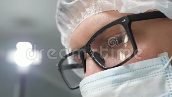 戴着手术面罩的眼镜的外科医生低头看病人然后站在监视器或助手旁边行动视频的预览图