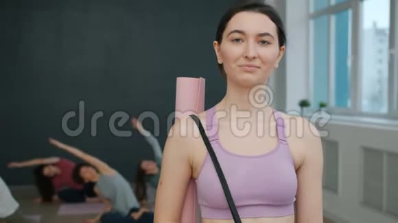 身着运动服的年轻黑发美女站在瑜伽馆微笑的肖像视频的预览图