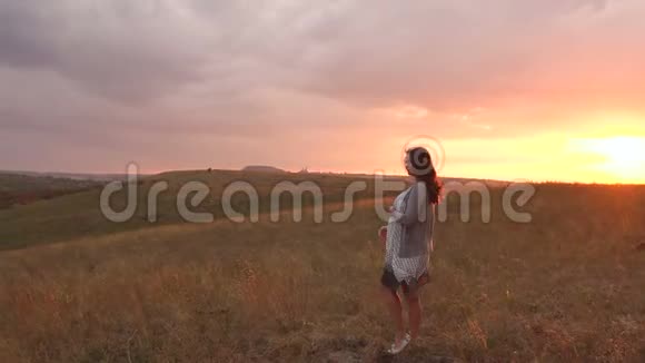 日落时分一位美丽的孕妇在一片狂风大作的田野上的剪影视频的预览图