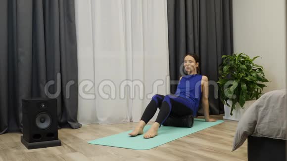 美女在瑜伽垫上用筋膜卷按摩臀部肌肉穿着蓝色上衣和紧身裤的年轻健康女性视频的预览图