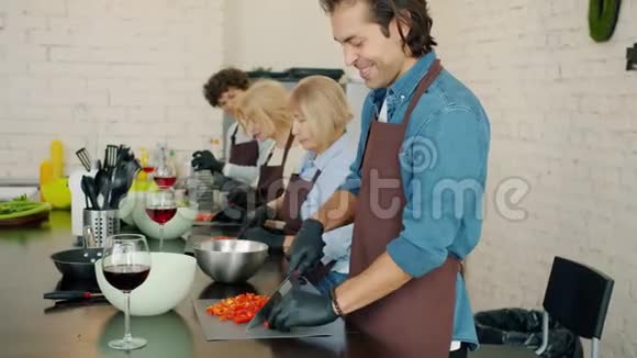 在烹饪课上穿着围裙在厨房里切蔬菜的快乐男人和女人视频的预览图