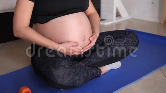 孕妇在家做运动的特写她轻轻地抚摸着她的胃视频的预览图