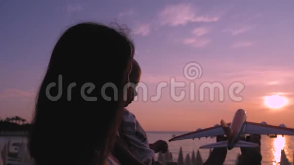 快乐的母亲和小儿子在日落时玩玩具飞机可爱的母子拥抱和玩玩具视频的预览图
