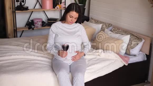 一个穿着睡衣的孕妇正端着一杯红酒坐在床上视频的预览图
