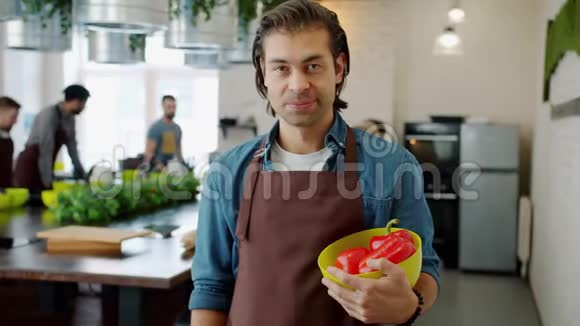 穿围裙的快乐男人微笑着在烹饪学校捧着一碗辣椒的画像视频的预览图
