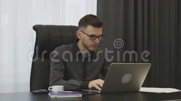 坐在办公室的人在笔记本电脑键盘上打字年轻自信的眼镜商人在现代办公室的电脑上工作男性视频的预览图
