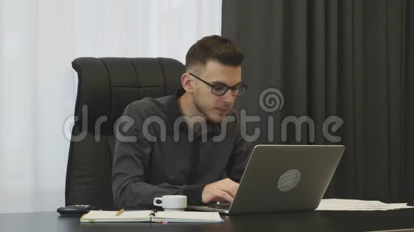 男人在办公室里用笔记本电脑键盘打字成功的商人在办公室工作电脑男性看手提电脑屏幕视频的预览图