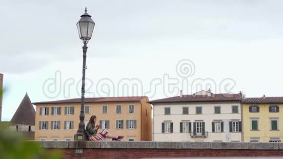 女人坐在路灯附近的栅栏上享受意大利冰淇淋总计划彩色房子在背景上视频的预览图