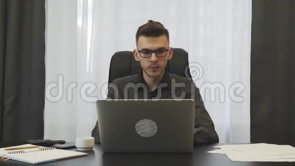 自信的年轻商人在办公室使用笔记本电脑戴眼镜的成功人士在工作场所使用电脑男性工作视频的预览图