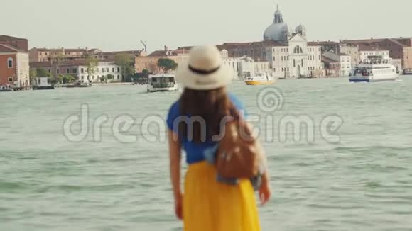戴帽子的女士站在大运河的码头上欣赏威尼斯的景色转身微笑视频的预览图