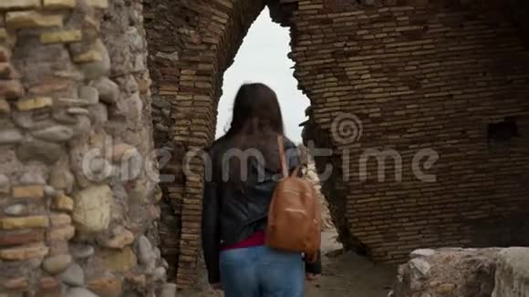 在意大利拉迪斯波利一名背着背包的旅游女孩穿过一座古老的堡垒托瑞弗拉维亚的废墟中的拱门后视图视频的预览图