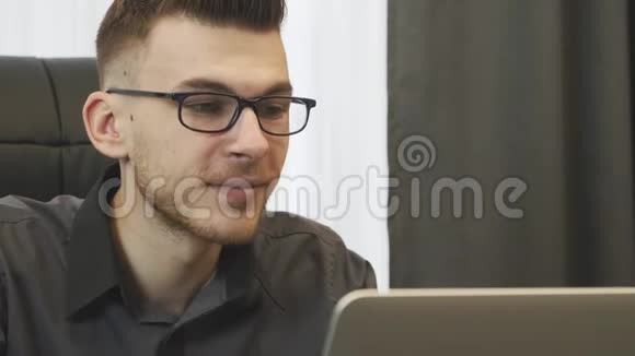 关闭办公室里用笔记本电脑工作的人戴眼镜的商人看电脑屏幕的肖像年轻自信的男性视频的预览图