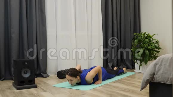 在家做健身和运动的妇女穿着潘通蓝衣服的年轻女性正在瑜伽垫上伸展专注的文莱视频的预览图