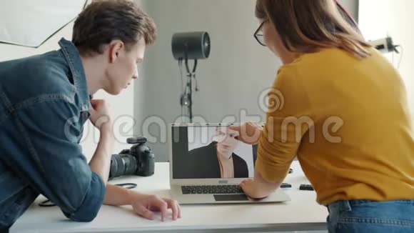 在演播室里男人和女人在笔记本电脑屏幕上讨论肖像照片的缓慢动作视频的预览图