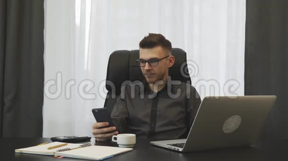 人在现代办公室工作年轻的成功商人戴着眼镜坐在办公桌前看电话男性经纪人支票视频的预览图
