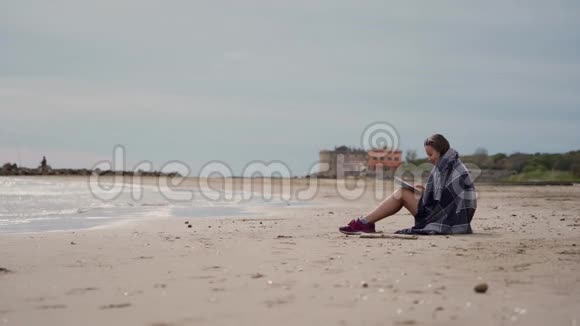 浪漫的女孩在凉爽的春天坐在海边看书侧视图视频的预览图